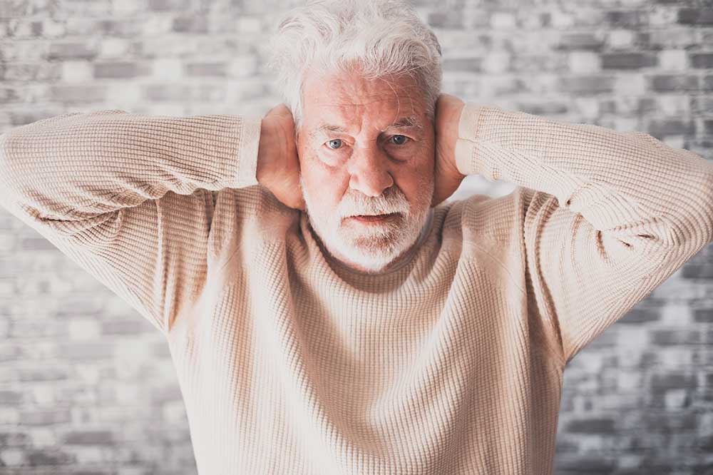 Older man covering both ears over a clogged ear feeling, a concern addressed at Hearing Care Professionals in Lafayette, IN